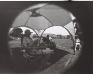 Black and white fish-eye lens film photograph, people sitting under a sun shade at the beach.
